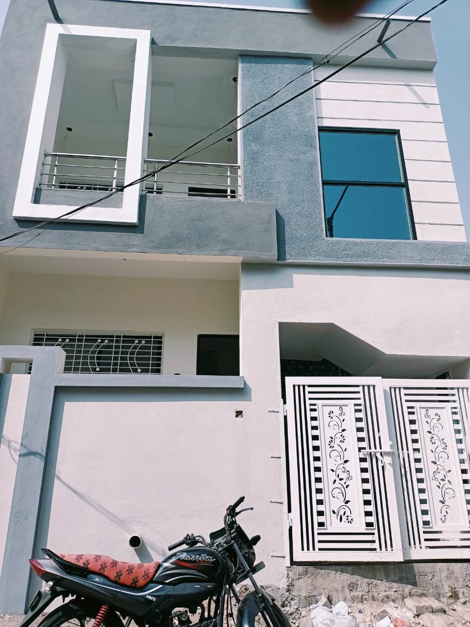 A completed two storey home built by Nisarg Infra, white and grey with a balcony and decorative gate